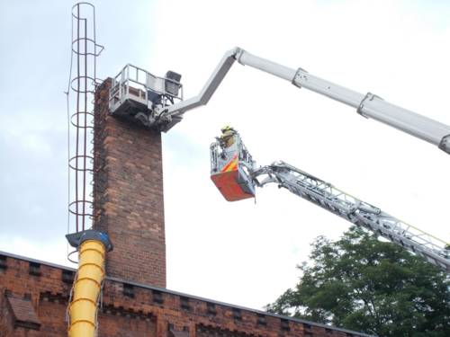 Ein Feuerwehrmann steht auf einer DRehleiter über einem Haus.